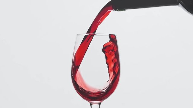 CU Red wine pouring from bottle into goblet. Close-up of rose wine pouring in wine glass over white background in slow motion. Central composition