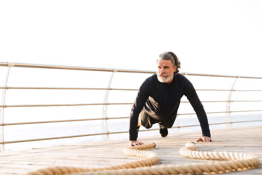 Image of sporty elderly man doing exercise with battle ropes