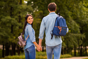 Behind view photo of cute pair groupmates walking dormitory hostel after lessons hold arms wear denim outfit