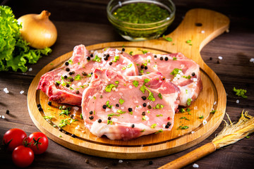 Seasoned raw pork chops, on top of circular wooden chopping board, next to cooking ingredients.
