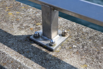 Closeup of a metal railing screwed tightly on concrete at a harbour pier