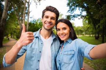 Portrait of lovely guy and girl with brunet haircut making photo showing thumb up sign wearing denim jeans shirt outdoors