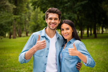 Portrait of lovely couple with brunet hair showing thumb up smiling wearing jeans denim shirts jackets outside in forest