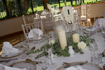 Luxury wedding reception dinning table setup with eucalyptus branches and gold geometric decoration on a rustic wooden chairs