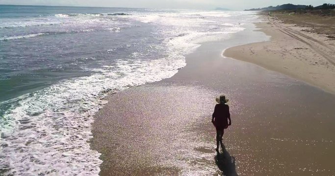 Dron sobrevuela a mujer que pasea de espalda en playa del paraiso