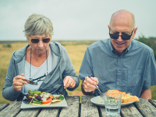 Senior couple eating lunch at picnic table outdoors