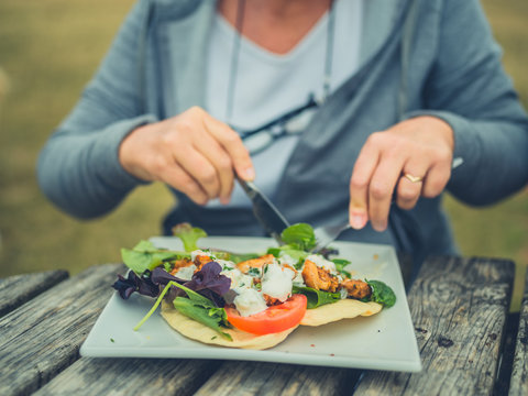 Senior woman eating salad  lunch at picnic table outdoors