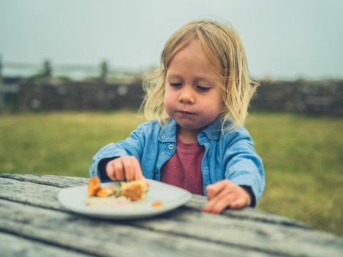 Little toddler eating lunch at picnic table outdoors