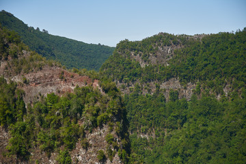 Naklejka premium Craggy mountains bathed in warm sunlight and covered in sparse greenery, peaking over the horizon, with sheer rock walls gleaming in the sun