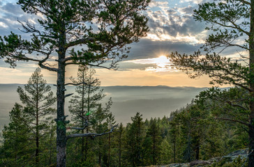 View from the mountain top over foggy Scandinavian mountains with wild pine tree forest, Sun shines with rays, mountain ridges, summer day with heavy dramatic clouds, North Sweden