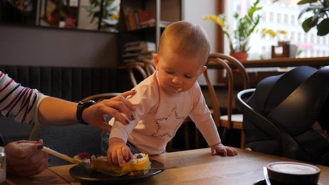 Clumsy baby try to put raspberry in a mouth suddenly drop in on a table and do it again mother and child daughter in cafe