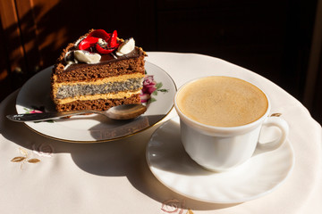 A cup of coffee with milk and a slice of cake with a flower of butter cream is a coffee break and dessert for the girl