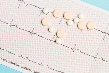 Electrocardiograma y pastillas medicamentos sobre fondo celeste. Vista superior. Concepto: Salud Medicina