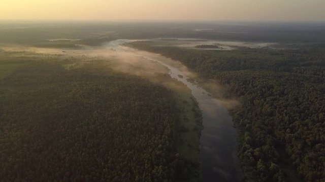 amazing valley covered with green thick forest crossed by long blue river and sparse fog at sunset bird eye view