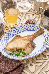 Fried fish flounder with parsley on white plate with glass of lemonade on oriental wooden table