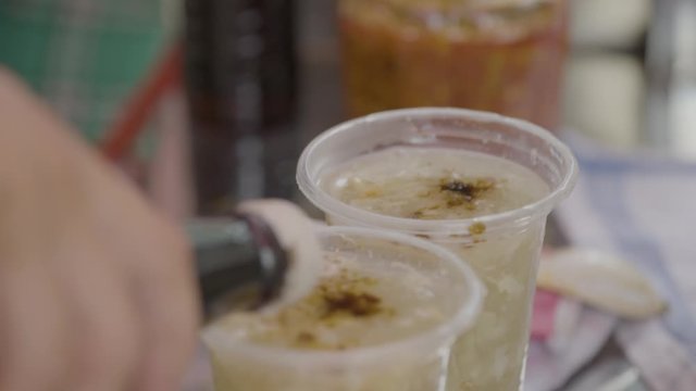 A daylight extreme closeup shot of a local vendor preparing servings of congee soup in transparent plastic disposable cups and garnishing it with chopped cilantro leaves..
