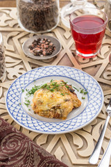 Baked meat with mushroom and mayo cheese sauce and glass of red drink on oriental wooden table