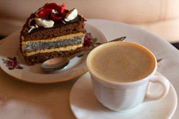 A cup of coffee with milk and a slice of cake with a flower of butter cream is a coffee break and dessert for the girl