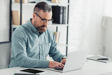 handsome businessman in shirt and glasses using laptop in office