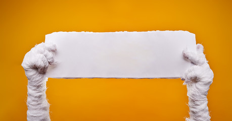 Photo of mummy's hands and empty blank paper on empty orange background .