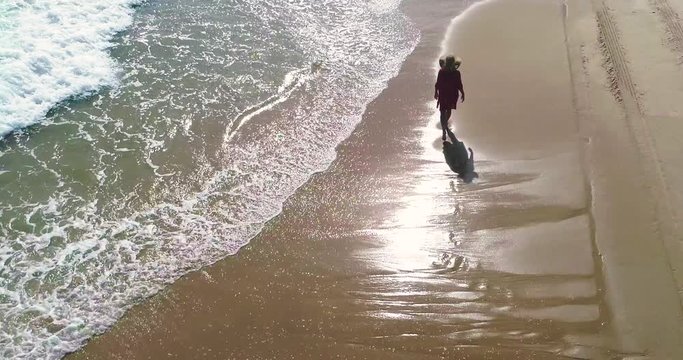 Dron sobrevuela a chica con sombrero que pasea por una playa dorada de arena