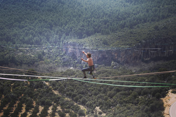 A man is walking along a stretched sling. Highline in the mountains. Man catches balance. Performance of a tightrope walker in nature. Highliner on the background of the mountains.
