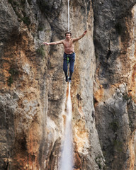 A man is walking along a stretched sling. Highline in the mountains. Man catches balance. Performance of a tightrope walker in nature. Highliner on the background of the mountains.