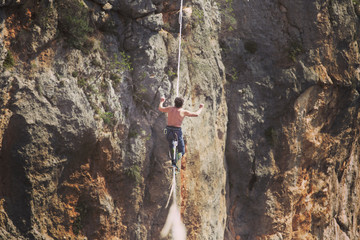 A man is walking along a stretched sling. Highline in the mountains. Man catches balance. Performance of a tightrope walker in nature. Highliner on the background of the mountains.