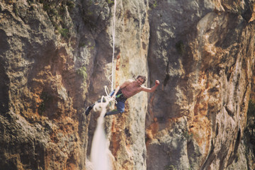 A man is walking along a stretched sling. Highline in the mountains. Man catches balance. Performance of a tightrope walker in nature. Highliner on the background of the mountains.