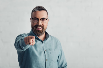 handsome businessman in shirt pointing with finger and looking at camera