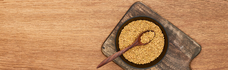 panoramic shot of bowl with grains and spoon in it on wooden cutting board