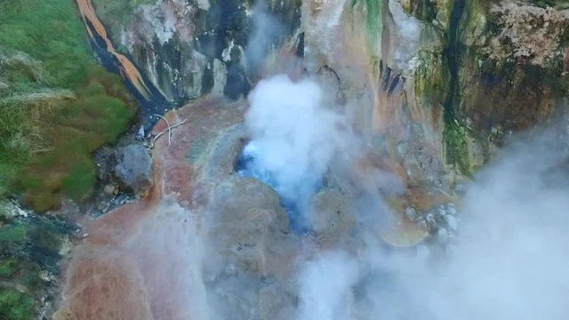 dense white steam over large hilly geyser surrounded by rocks and green meadows vertical upper view
