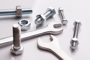 Wrench and nuts with bolts. Scattered bolts and nuts on a white glossy background.