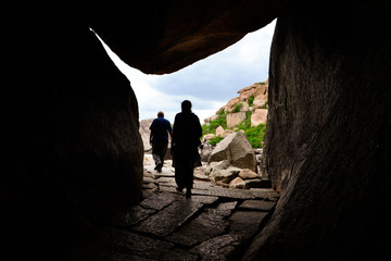 people walking through cave of stone in Hampi