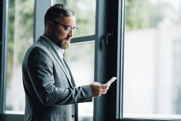 handsome businessman in formal wear and glasses holding smartphone