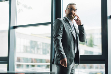 Fototapeta premium przystojny biznesmen w wizytowym i okularach rozmawia na smartfonie