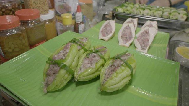 A closeup shot of stuffed bitter gourd (Canh Kh? Qua Nh?i Th?t) on display on top of a plastic banana leaf tray along with the rest of other local delicacies in a street food stall..