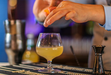 Fototapeta na wymiar Cocktail on a bar in a tall glass and a bartender putting garnish.