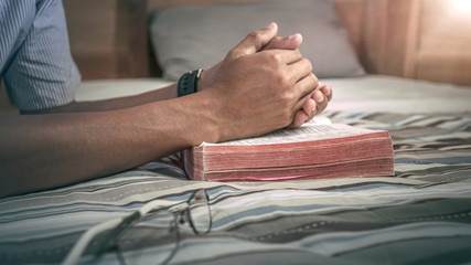 Close up Bible with hands of man praying in bed. christian praying concept.