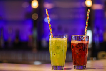 Cocktails red and green at a bar. Non alcoholic fruit mocktails in glasses with straws.