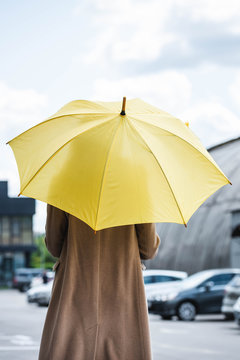 Back view of woman in coat holding yellow umbrella