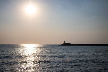 Fototapeta na wymiar Light house at sunset. Sun rays reflecting on the water of the sea.