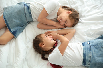 Obraz na płótnie Canvas Portrait of cute twin girls lying on bed, top view
