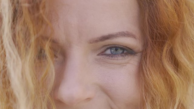 Extreme close-up face of mature red-haired woman with curly hair smiling happily looking at camera. Natural beauty concept. Emotions, happiness, good mood