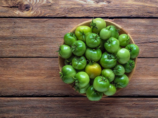 Green tomatoes in a bowl on a wooden table. Top view.