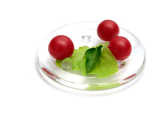 A close up of three cherry tomatoes, lettuce and a leaf of basil on white
