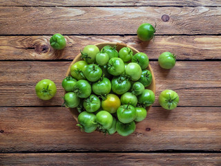 Green tomatoes in a bowl on a wooden table. Top view.
