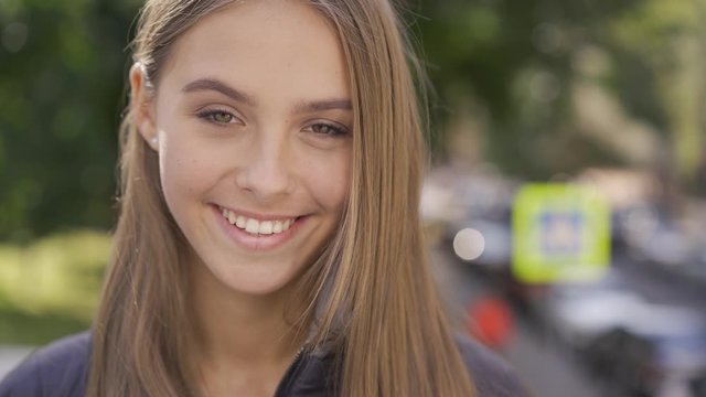 Close-up of attractive young caucasian woman with long brown hair smiling happily looking at camera. Emotions, happiness, good mood.