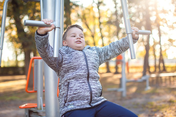 Kid boy does workout on trainer equipment outdoor. Children, sport, activity and healthcare concept