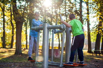 Two boys do workout on trainer equipment outdoor. Children, sport, activity and healthcare concept
